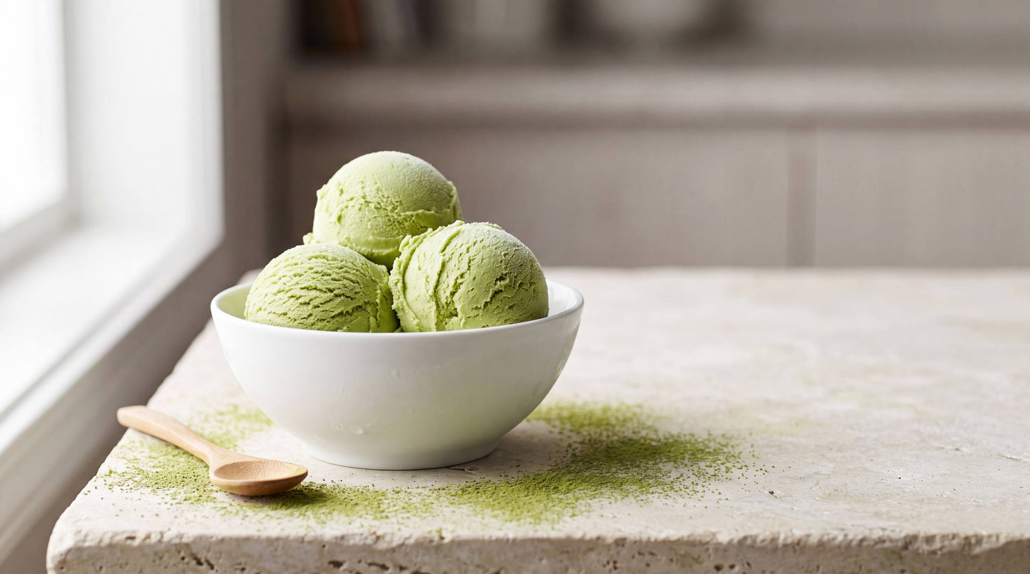 Scoops of creamy green matcha ice cream in a bowl with a small dusting of matcha powder