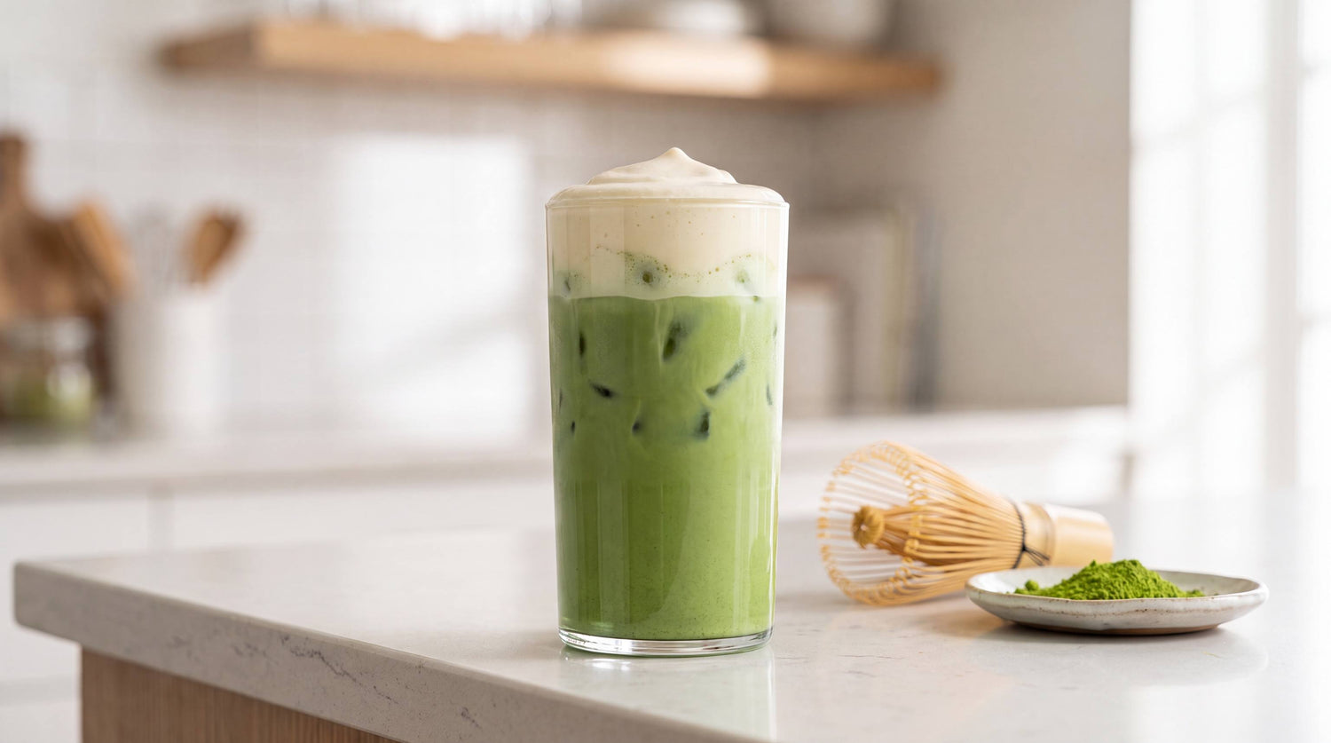 Tall glass of iced matcha with a thick pale cold foam floating on top of the green base over ice