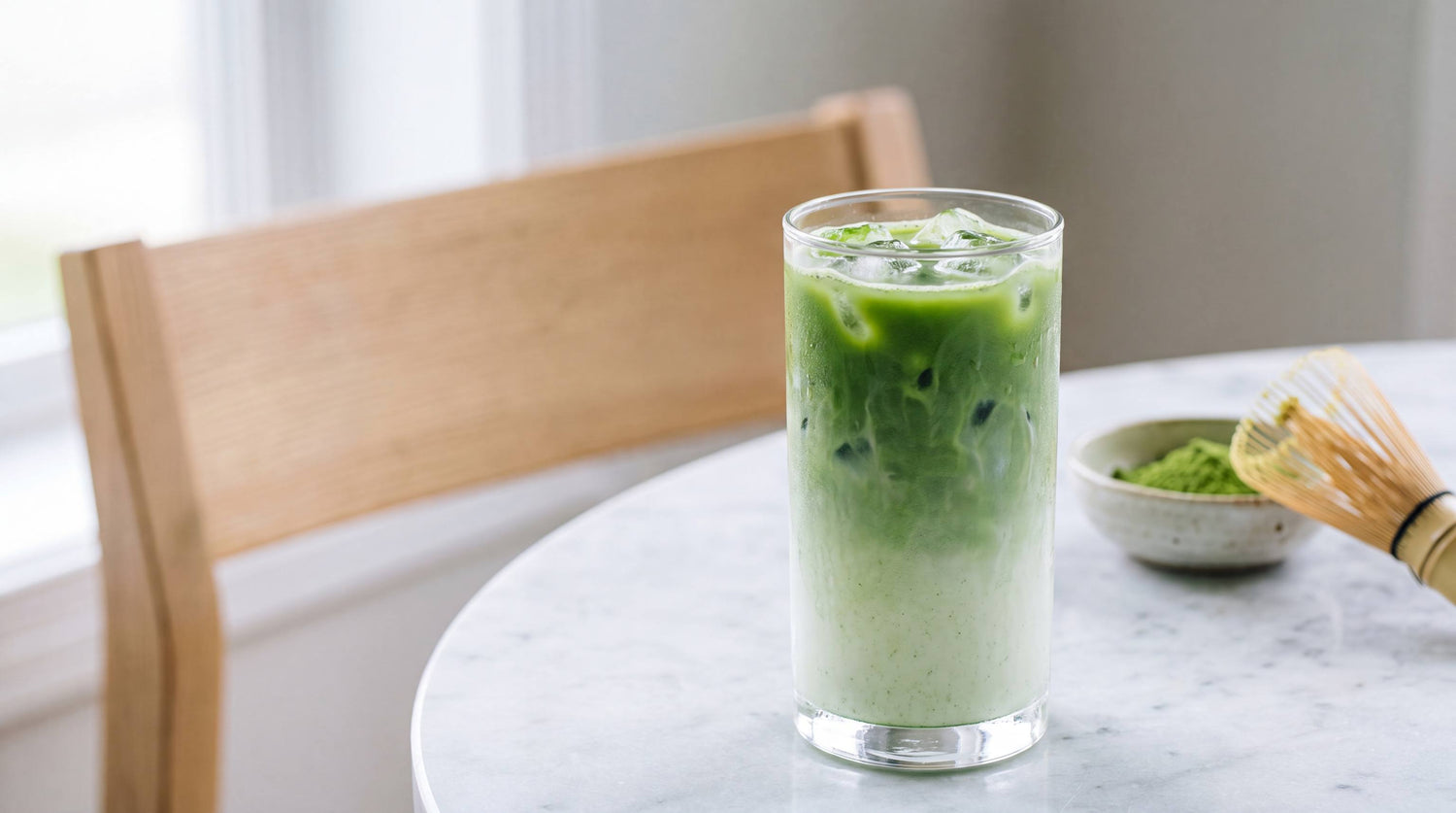 An iced matcha latte in a tall glass, vivid green matcha poured over milk and ice