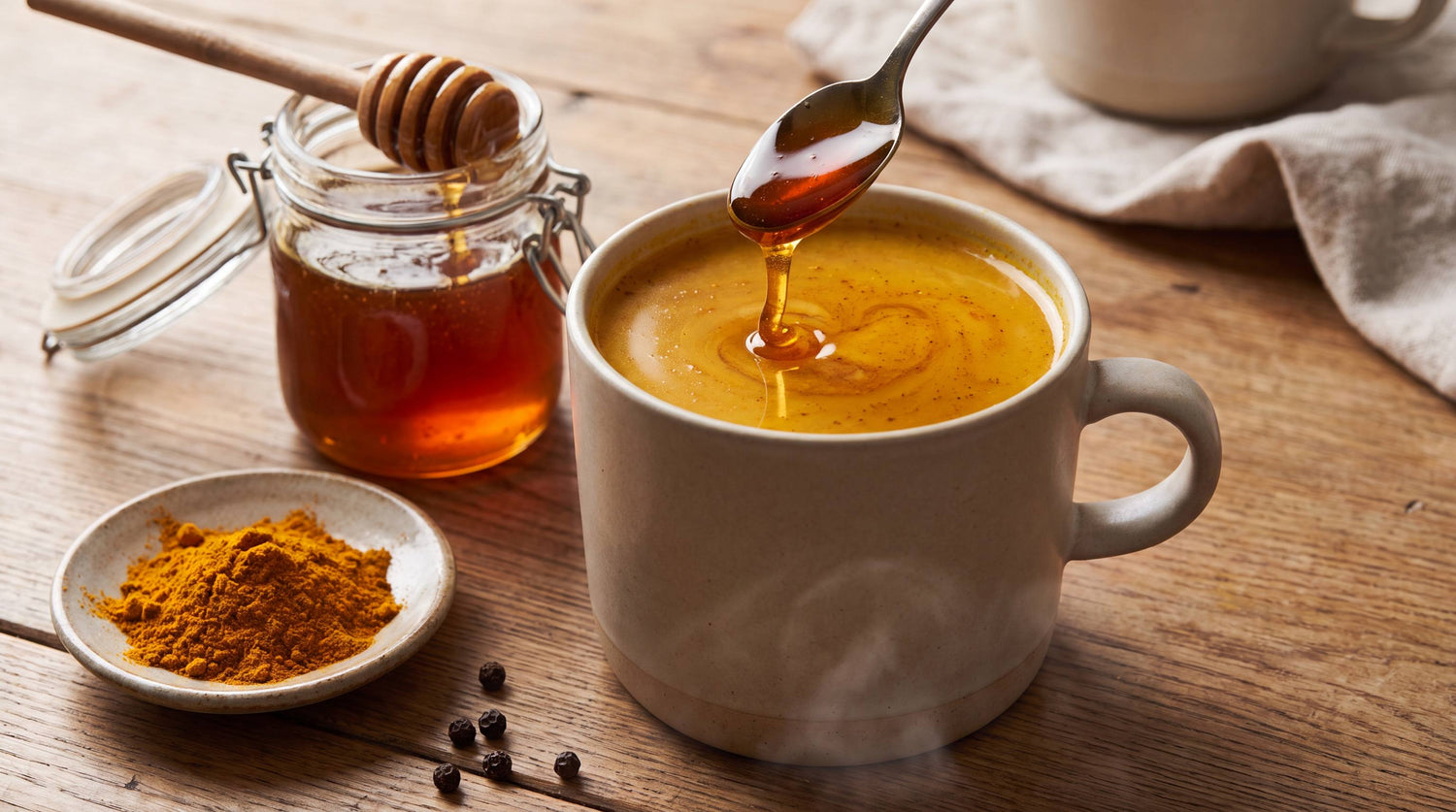A mug of golden turmeric tea with raw honey being stirred in with a spoon